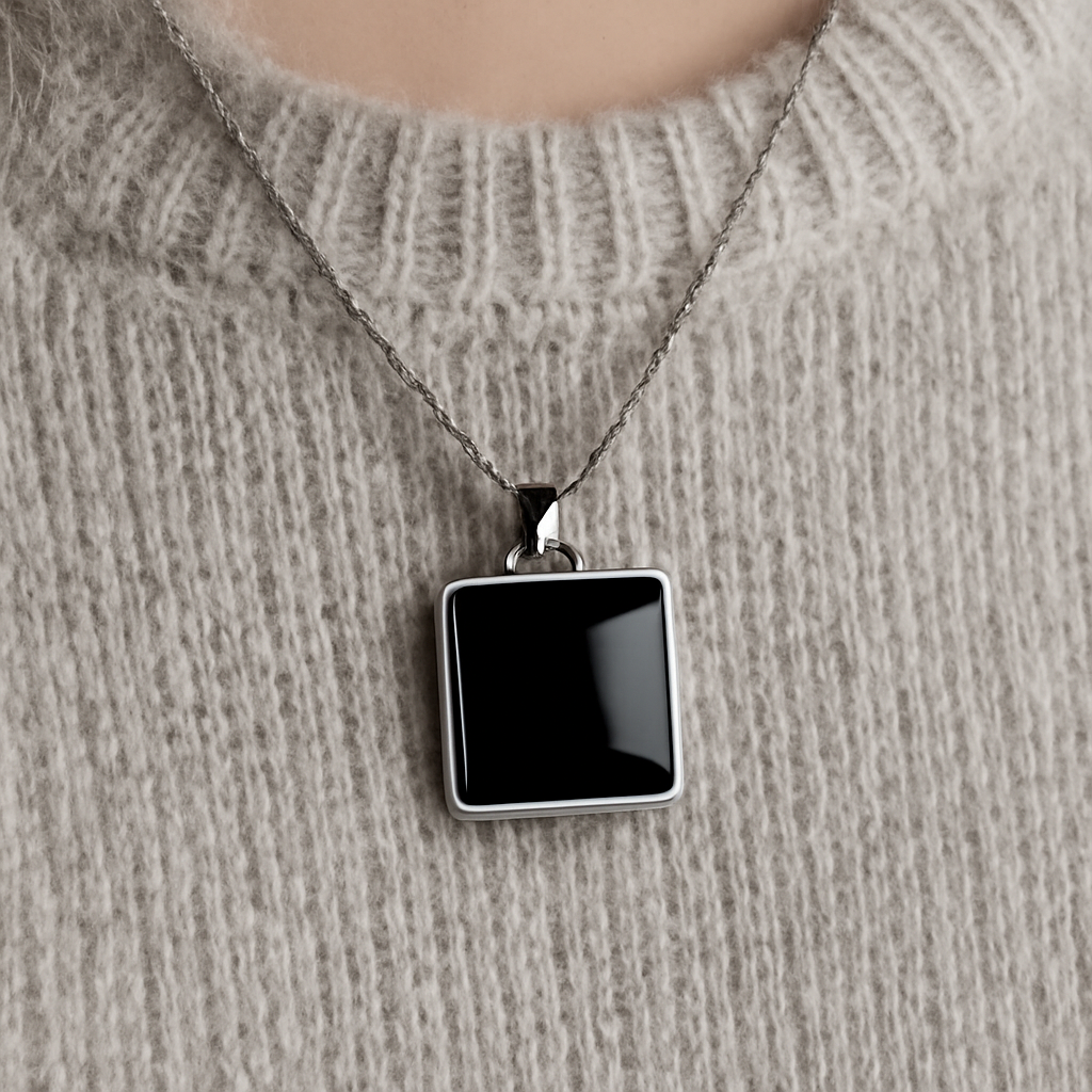 A close‑up of a black onyx square pendant necklace against a soft grey sweater, showing the deep black stone and sleek square metal setting. Alt: Black onyx square pendant necklace styling example.