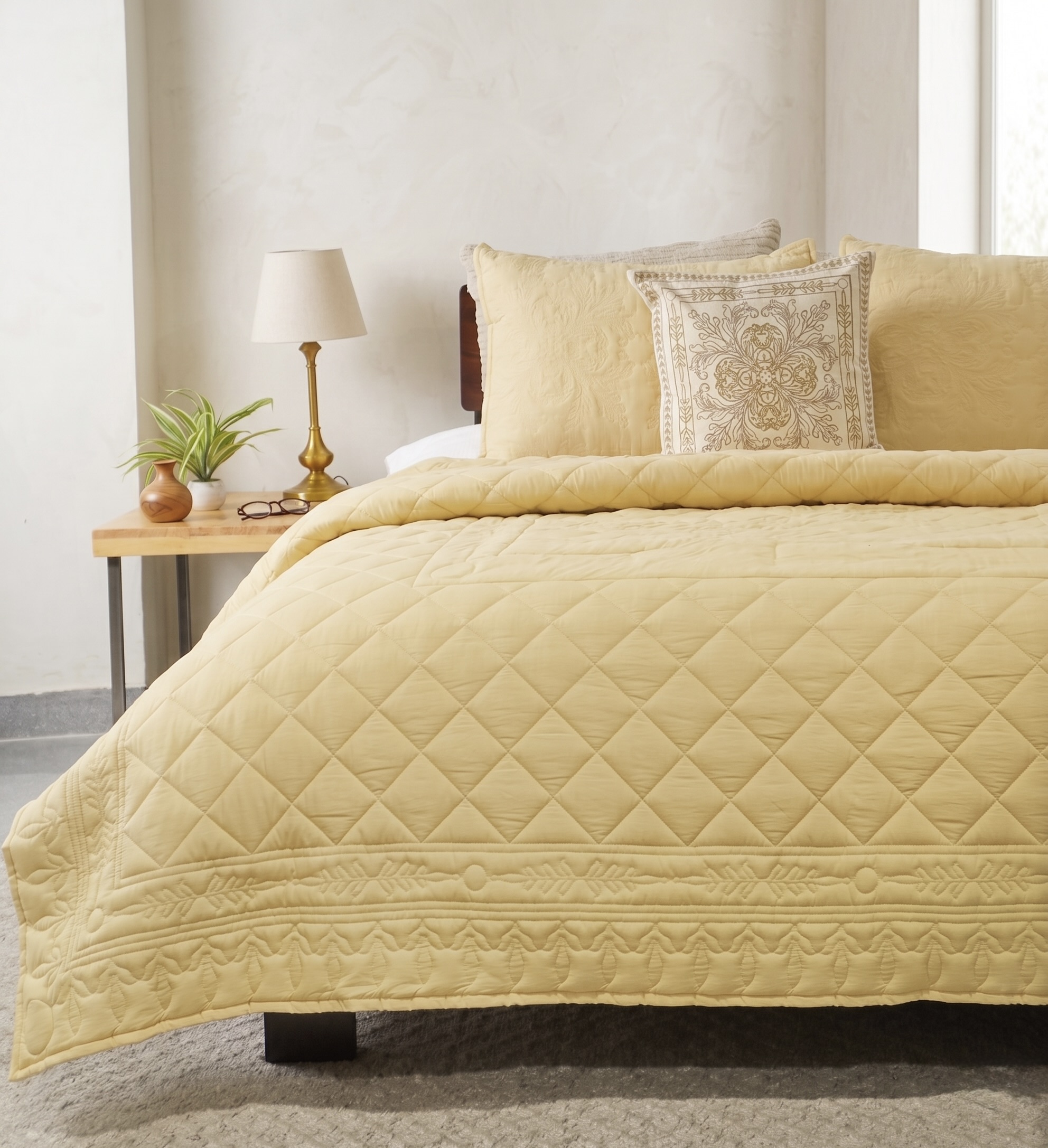 Marigold yellow cotton quilt with engineered diamond quilting and a quilted floral border, with matching shams and an embroidered cushion