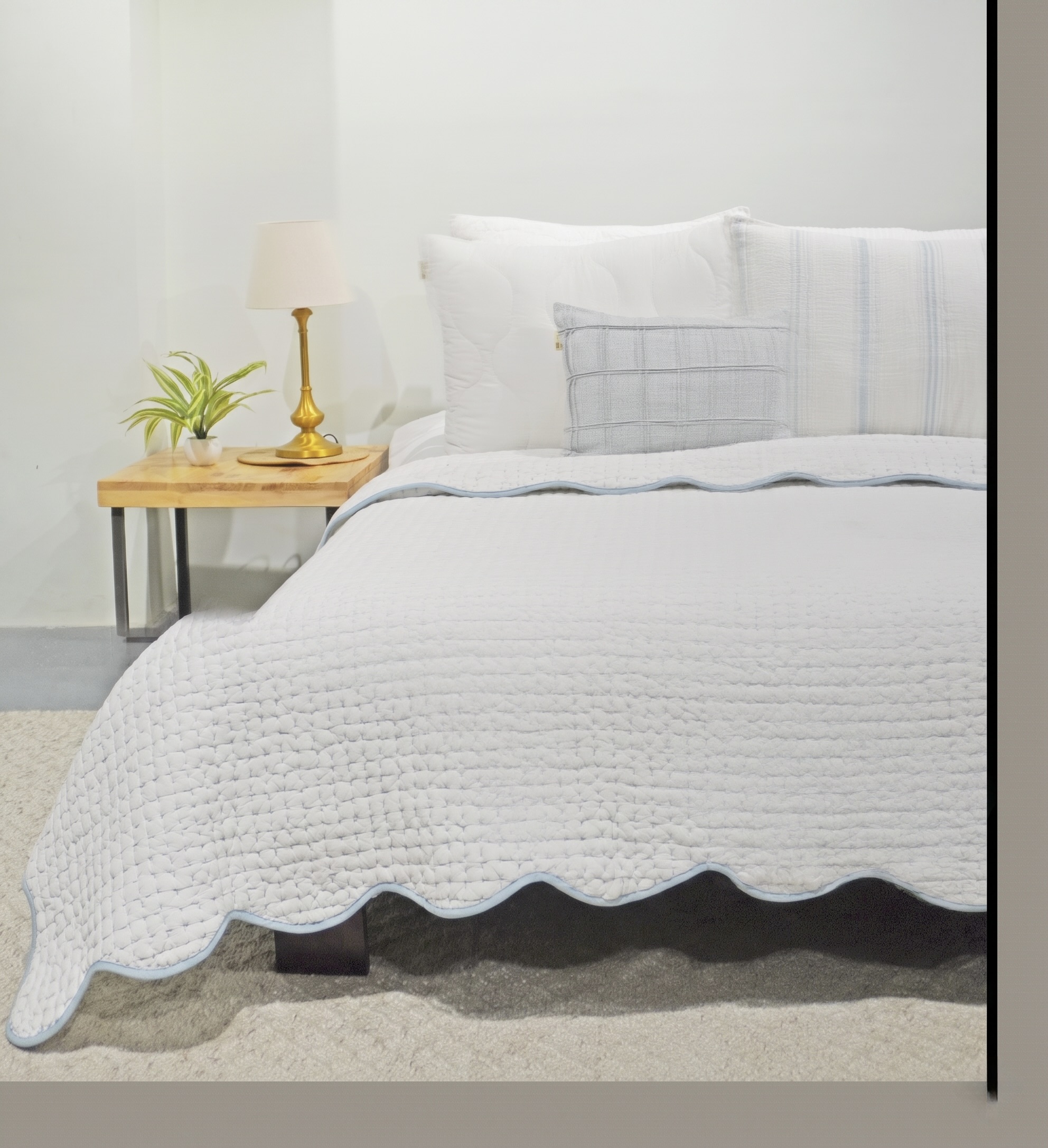 White hand kantha quilted coverlet with a scalloped edge trimmed in sky blue, on a bed with white pillows and a checked cushion