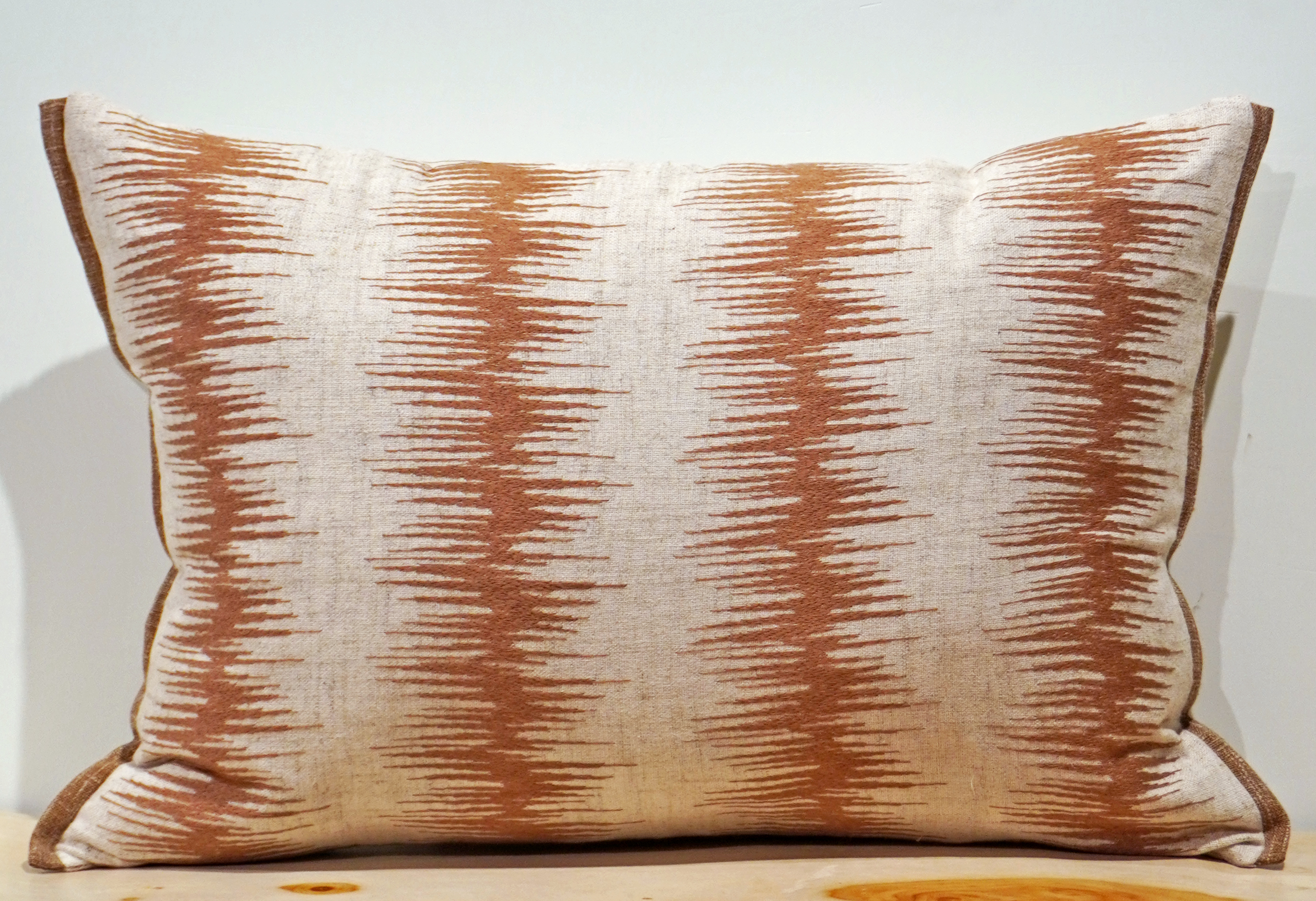 Natural linen lumbar pillow cover with vertical columns of rust terracotta embroidery in a feathered ikat-style stripe and a rust edge