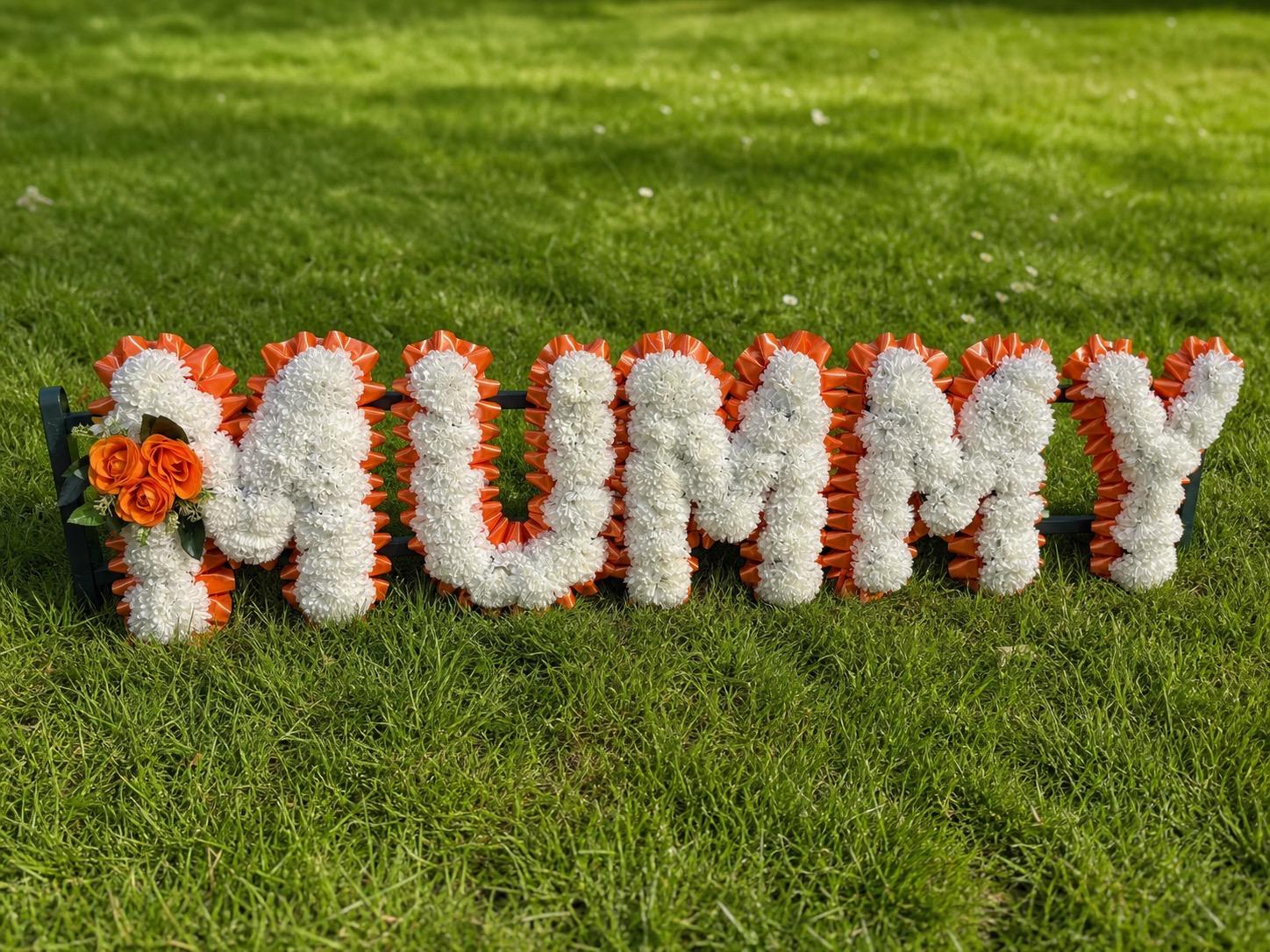 Heart-shaped silk funeral flowers beside Gates of Heaven cemetery entrance.