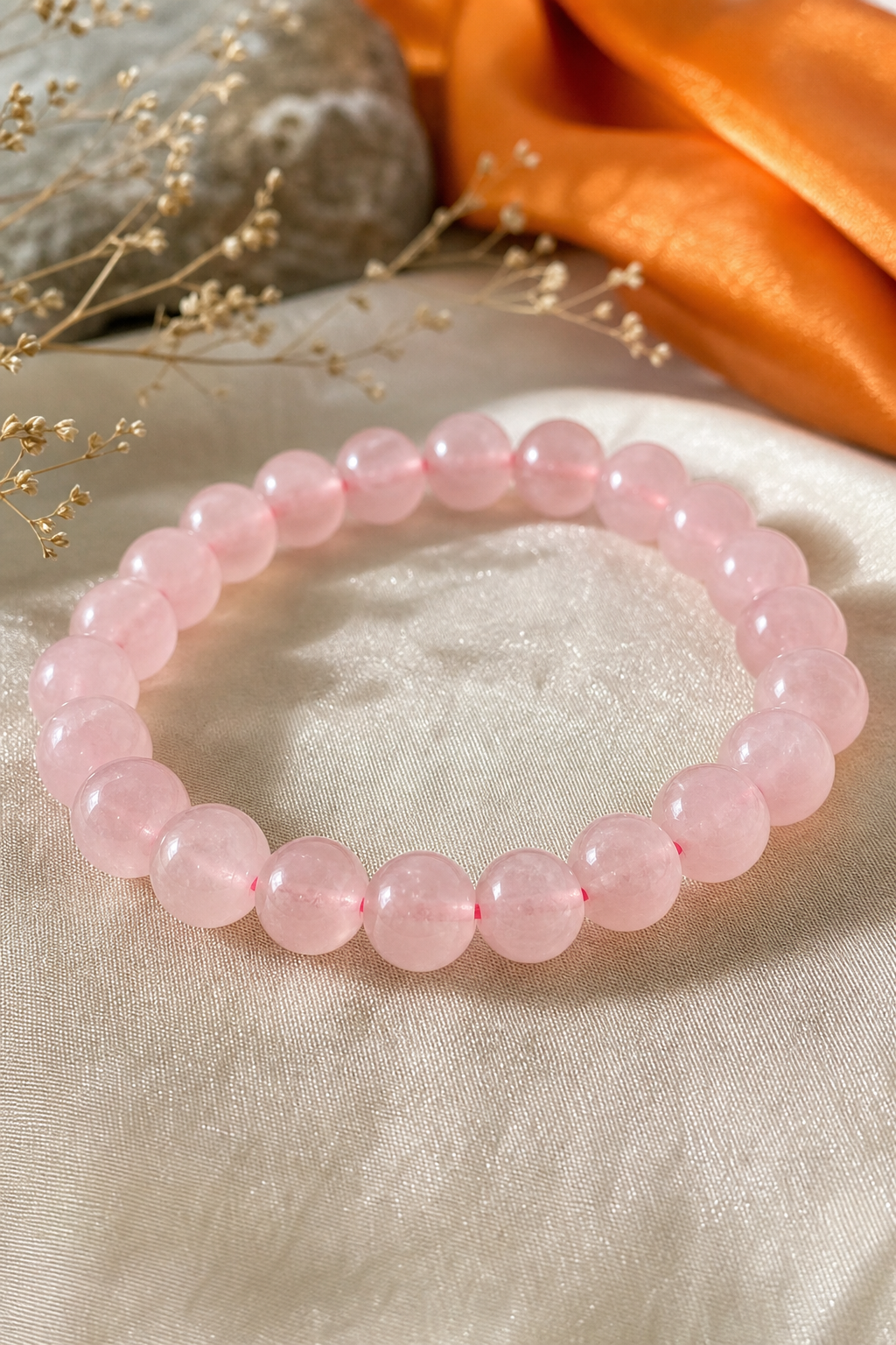 A realistic close‑up of a pink rose quartz bead bracelet on a soft fabric background, showing the smooth beads and stret