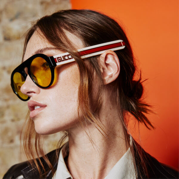 A high‑resolution, realistic photograph of a stylish woman trying on vintage designer sunglasses in a London boutique, s