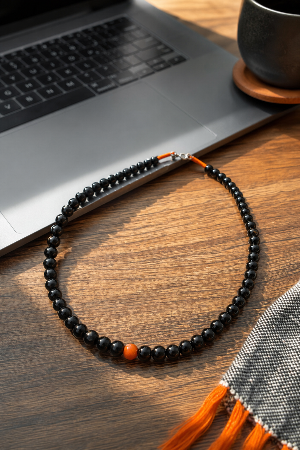 A photorealistic closeâup of a 19âinch black tourmaline bead necklace laid on a wooden table beside a laptop, soft natural light highlighting the deep black luster. Alt: black tourmaline protective necklace for EMF shielding.