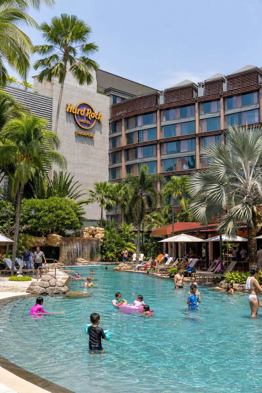 A photorealistic wide shot of the Hard Rock Hotel Singapore's outdoor pool area with kids splashing and families relaxing under tropical palms. Alt: Hard Rock Hotel Singapore family pool area at Resorts World Sentosa.