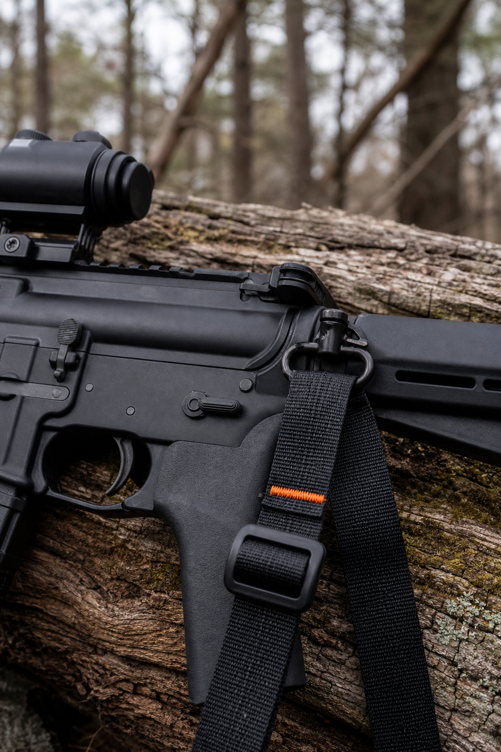 A realistic close-up of a tactical sling attached to an AR-15, showing the low-profile slider and quick-detach swivel against a woodland background. Alt: Tactical sling on AR-15 with quick-detach swivel
