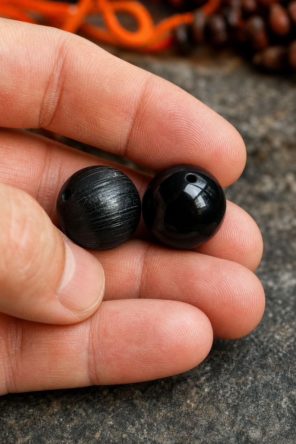 A close‑up of a hand holding two black beads, one genuine tourmaline with visible striations and one dyed onyx, set against a neutral background. Alt: spotting real black tourmaline beads