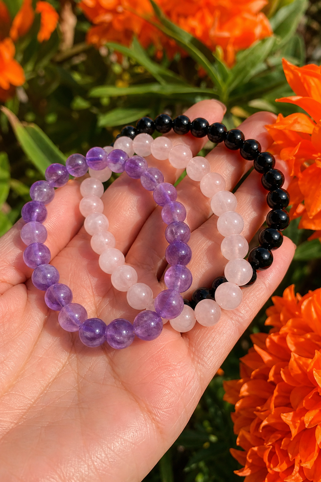 A close-up photo of a hand holding several gemstone bracelets in natural sunlight, showing the sparkle of amethyst, rose quartz, and black onyx. Alt: Handcrafted crystal bracelet gift ideas from Auras of Osiris.