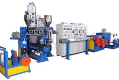 A realistic photo of a factory floor with a crosshead extrusion line, showing a technician inspecting a cable coating process. Alt: Crosshead extrusion line in cable manufacturing.