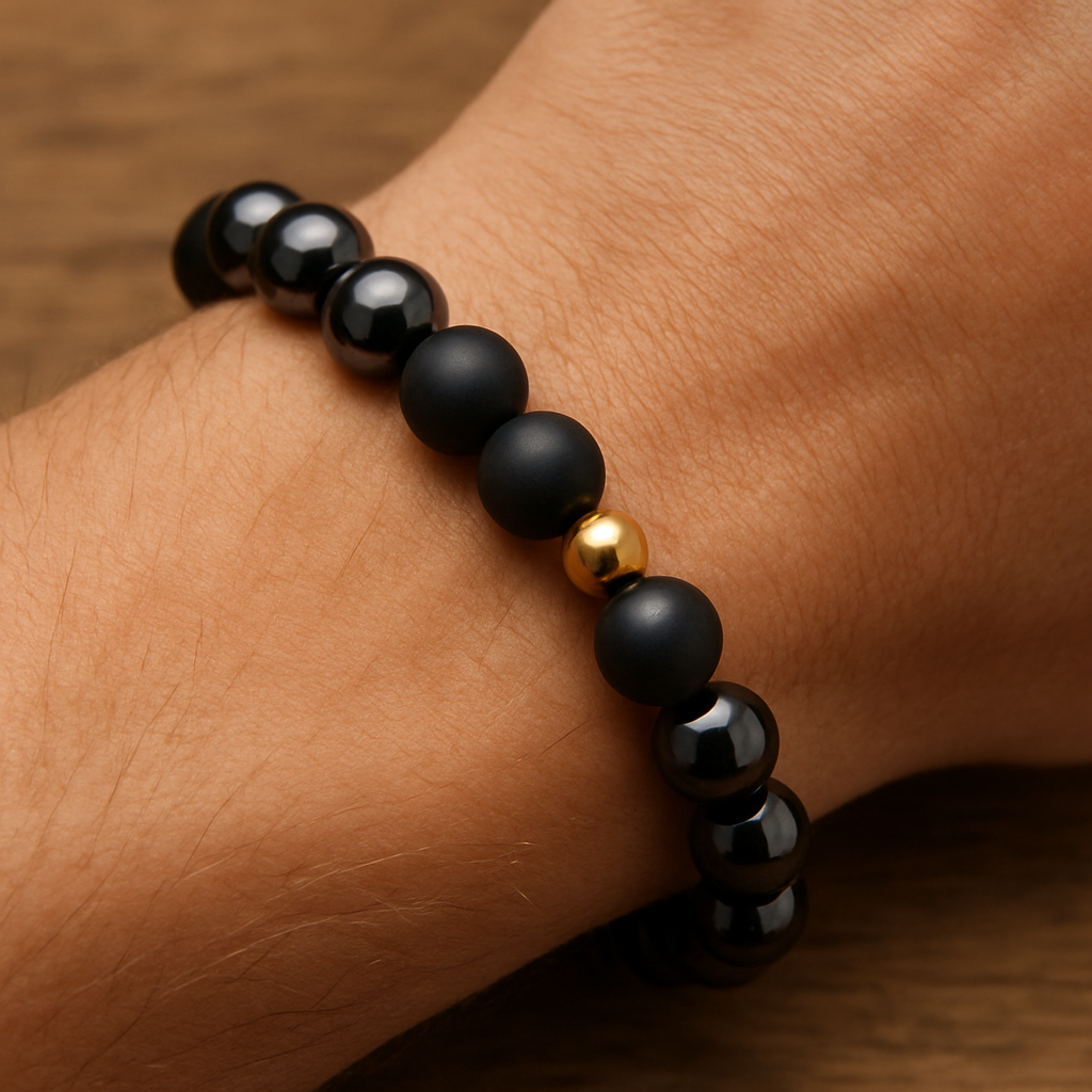 A close‑up of a handcrafted hematite bracelet on a wooden wrist, showcasing both glossy and matte beads with a small golden accent bead. Alt: Hematite bracelet styling guide showing size, finish and focal bead options.