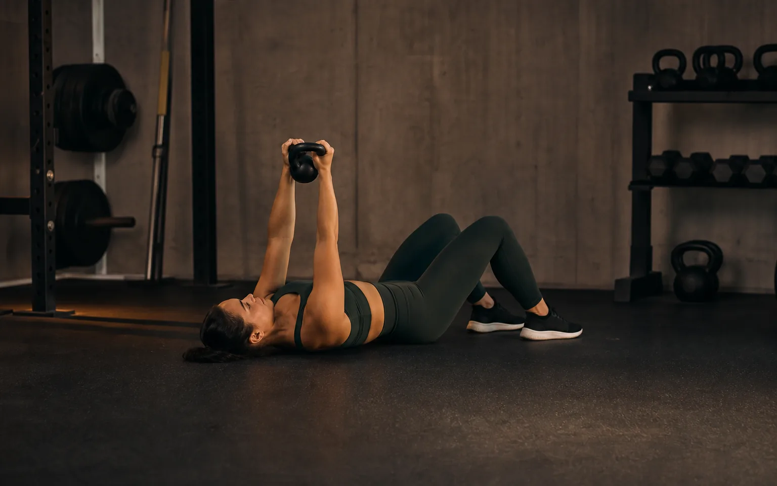 A woman presses a kettlebell with both hands holding its horns close together.