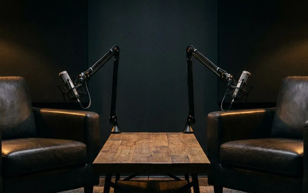 Illustration of an empty two-chair podcast studio set with boom microphones