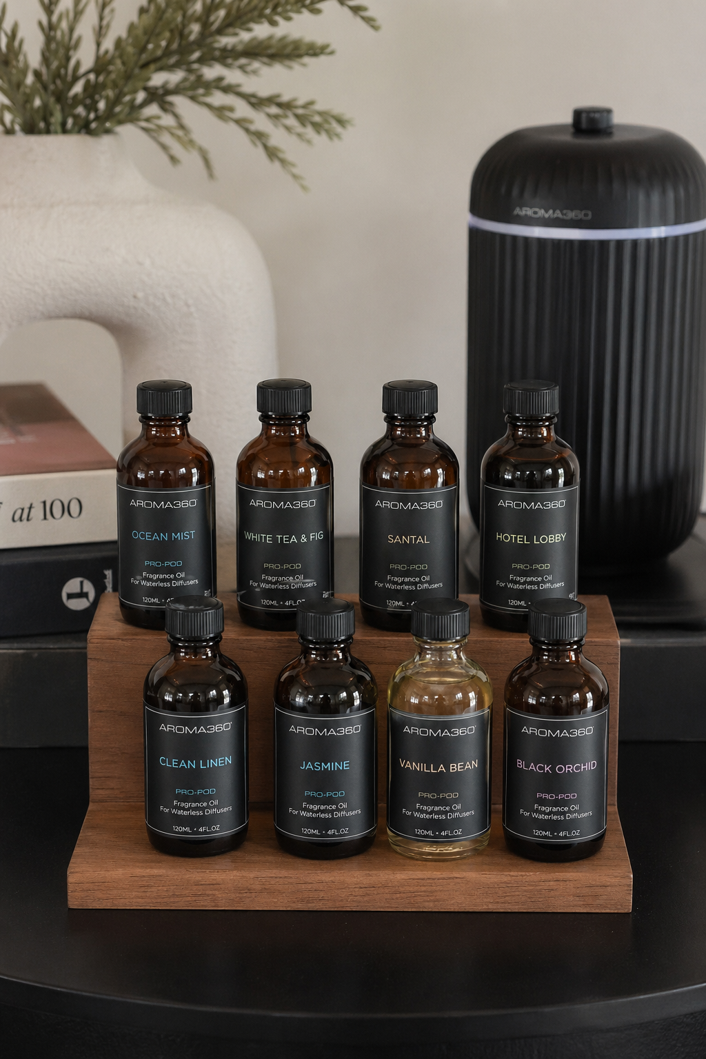 A photorealistic collection of small glass bottles containing essential oils and fragrance blends on a wooden tray, with a diffuser in the background. Alt: Essential oils and fragrance blends for waterless scent machines